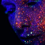 Face under UV light with glowing reflected multicoloured dots on it
