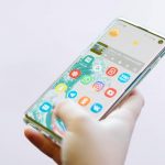 A hand holds a smartphone displaying apps representing whether to choose apps or website for your platform