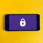 Mobile phone showing purple screen with white locked icon photographed agains a yellow background