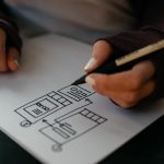 Writer draws infographic diagram on white sheet of paper while holding pen