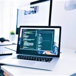 Laptop open on desk in office displaying software code