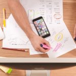 Aerial view of workdesk with screen papers mobile phone and hands making notes