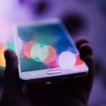 Hand holds mobile phone with multicoloured circles reflecting off its screen
