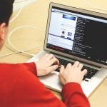 Software programmer types into laptop showing software code on screen