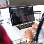 Software developer writes code into laptop on a desk