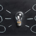 A lightbulb rests on a blackboard with drawings of circles around it denoting ideas