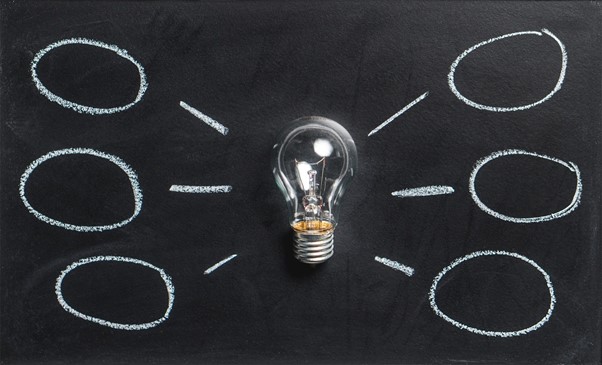 A lightbulb rests on a blackboard with drawings of circles around it denoting ideas