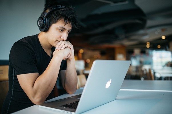 Man sits in front of laptop screen with headphones on his head inside an office with a view of a nightscape