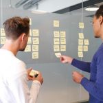 Product manager talks to product owner in front of a project planning board in an office