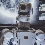 Robot stands before a screen showing a planet and software screens