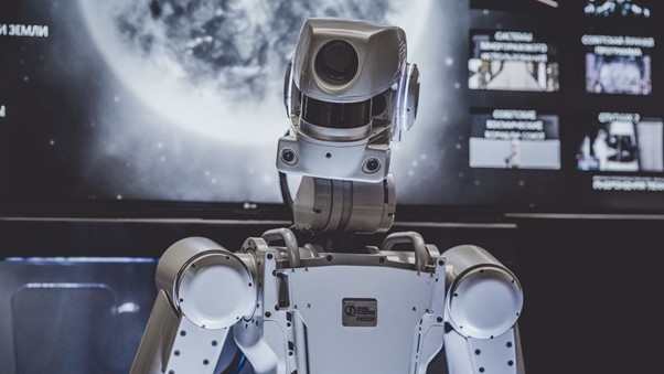 Robot stands before a screen showing a planet and software screens